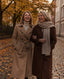 Two friends in autumn coats walking on a leafy street